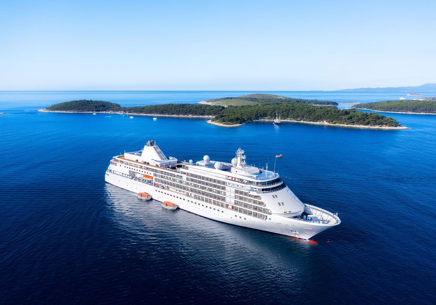 A white cruise ship sailing in deep blue water near lush, green islands under a clear sky.
