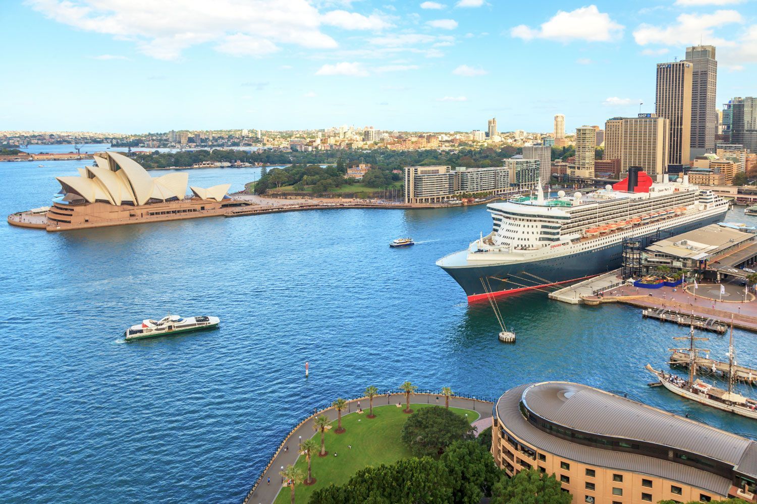 A high-angle view of Sydney Harbour with the Opera House on the left and a large cruise ship docked at the pier.