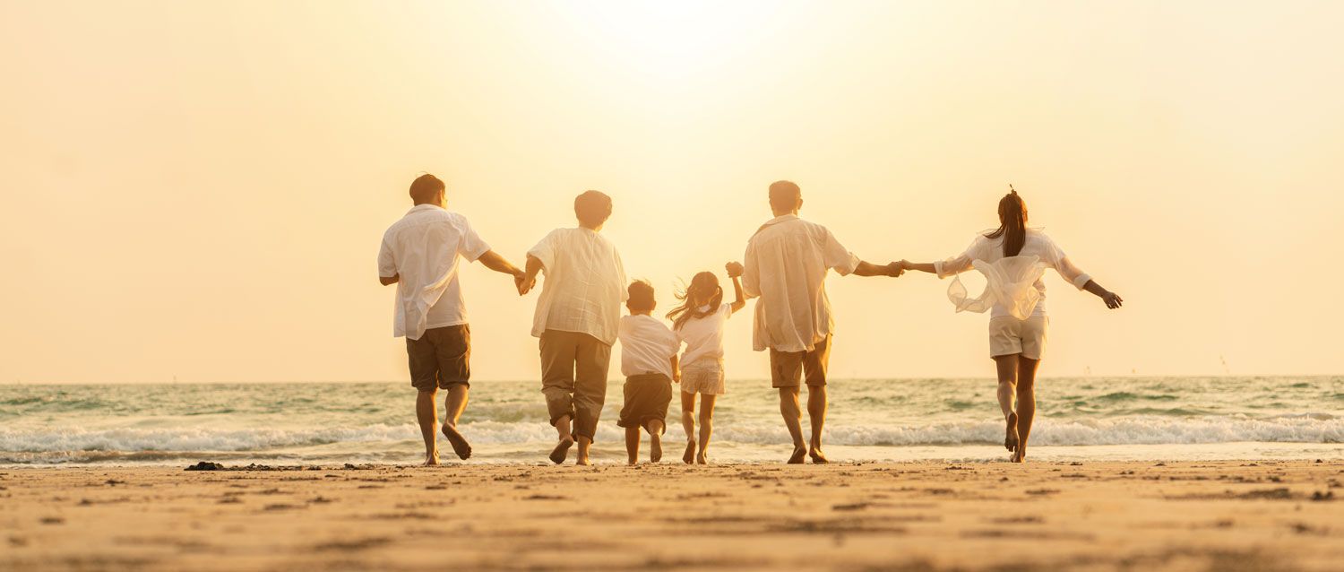 Six people holding hands and walking toward the ocean at sunset.