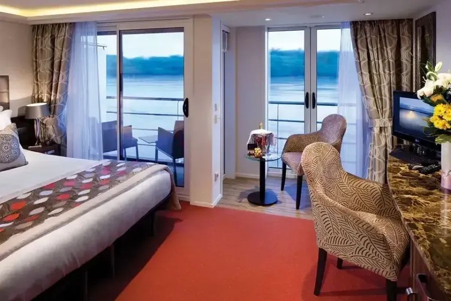 A hotel suite featuring a king bed, red carpet, and a balcony with sliding glass doors overlooking a body of water.
