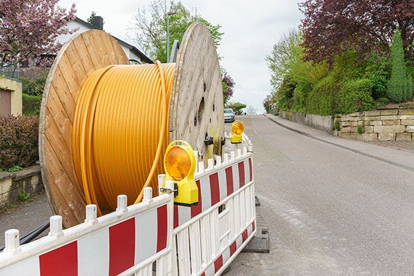 A large spool of fiber optic cable is sitting on the side of a road next to a fence.