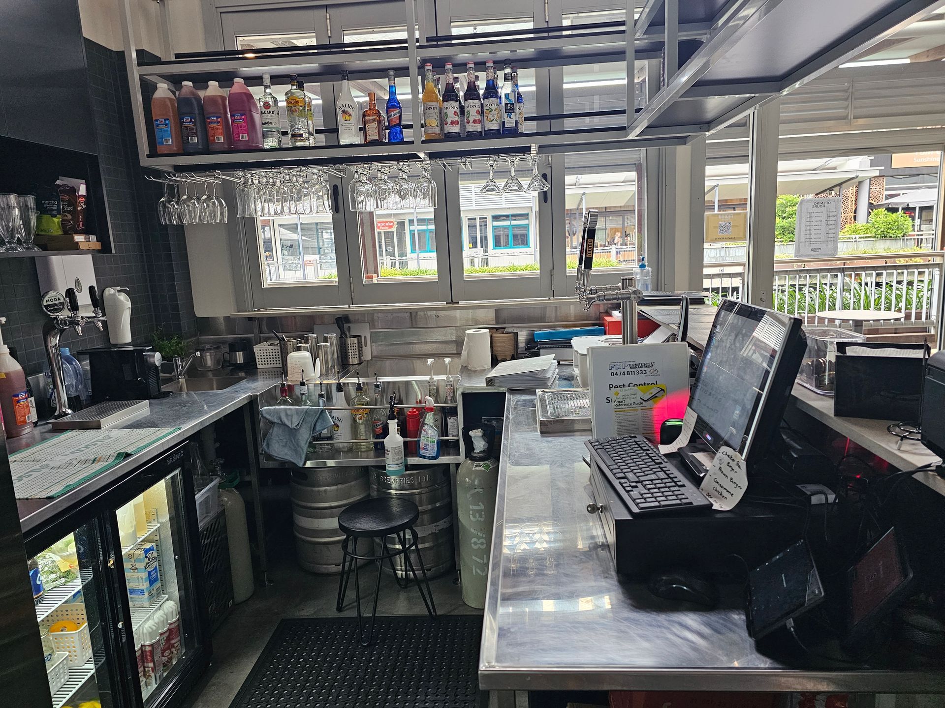 A kitchen with a lot of bottles on the shelves and a computer on the counter.