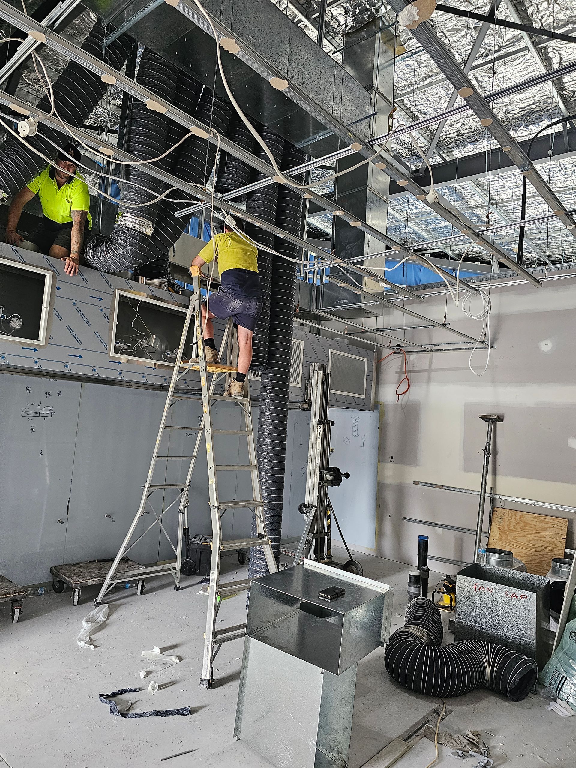 A man on a ladder is working on the ceiling of a building.