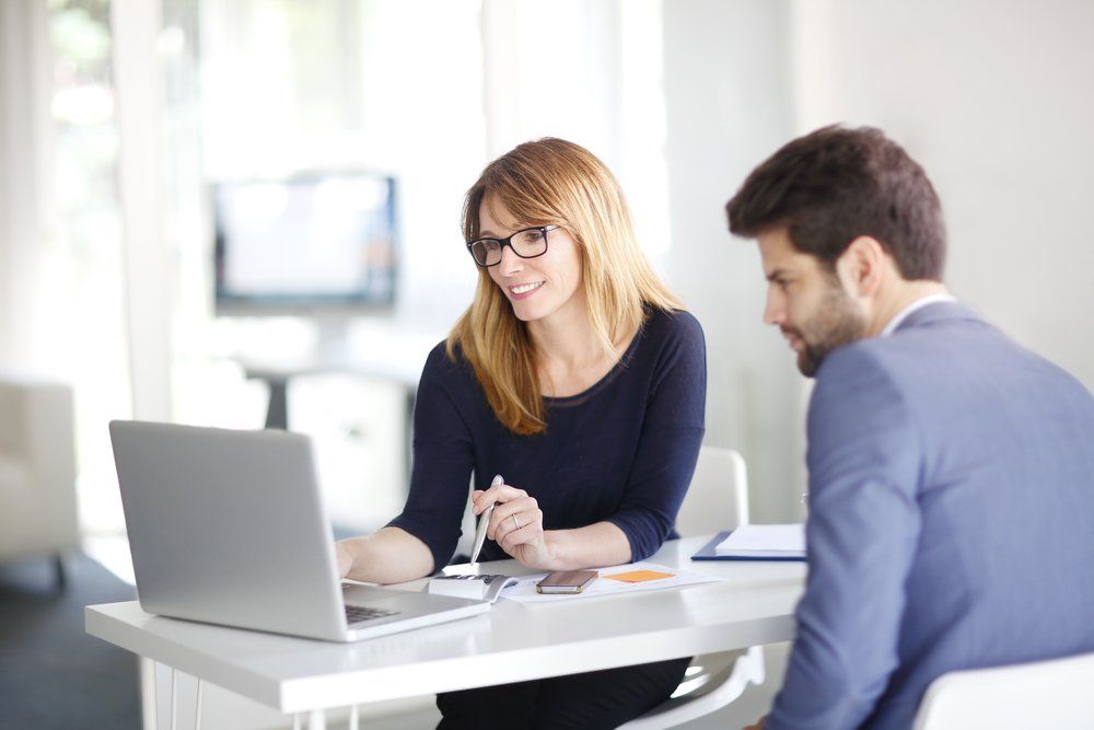 Businesswoman investment advisor sitting at computer in office chatting with young professional man