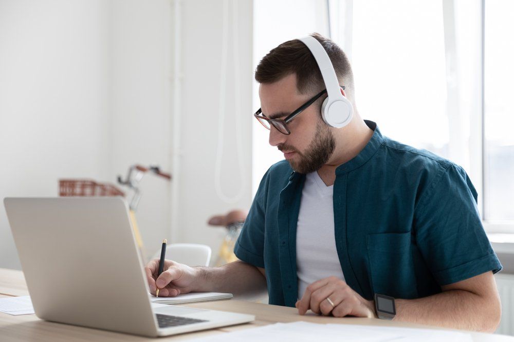 In spectacles, a focused young businessman corporate worker employee wears wireless headphones.