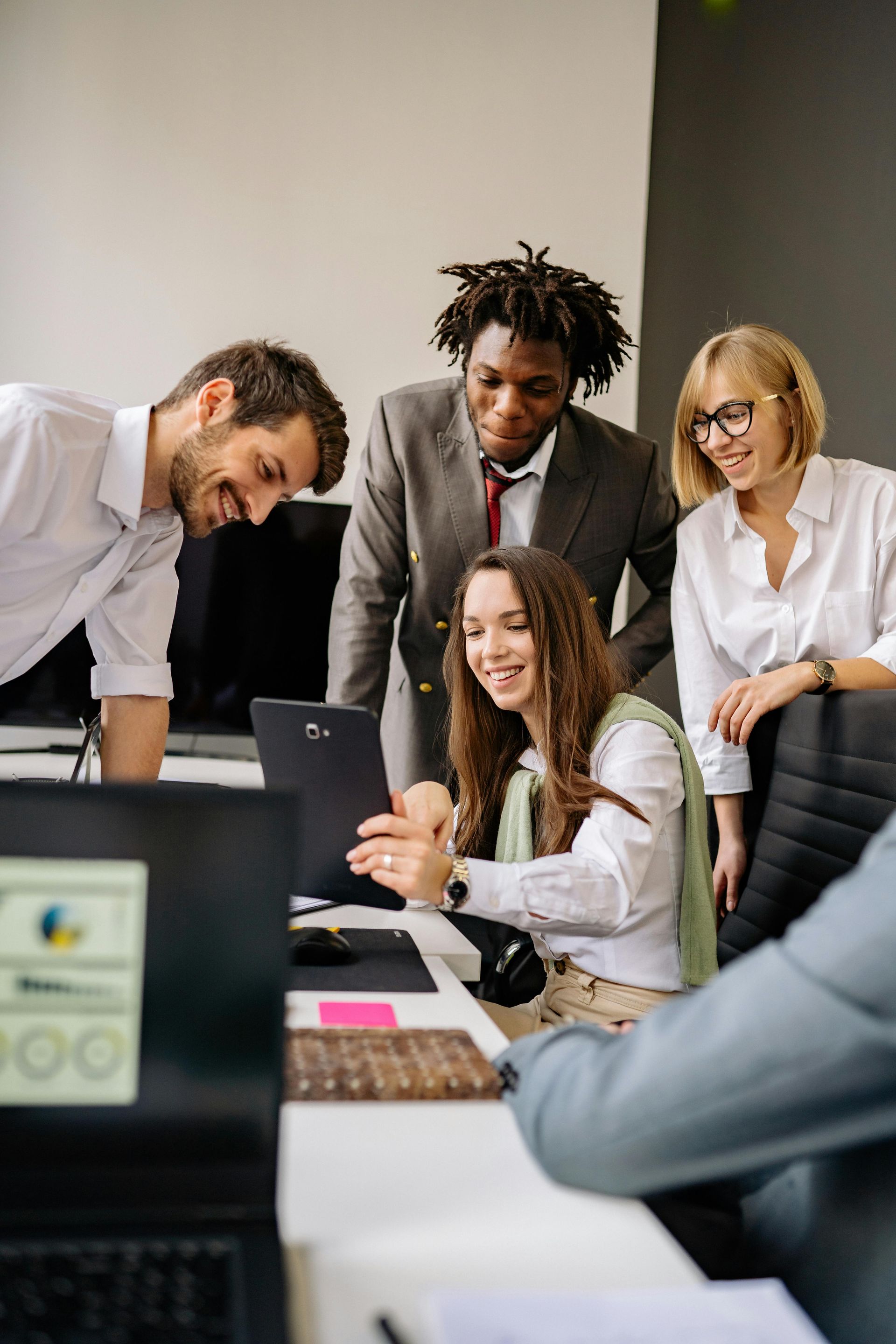 Team gathered around a laptop in a bright office, discussing work and smiling.