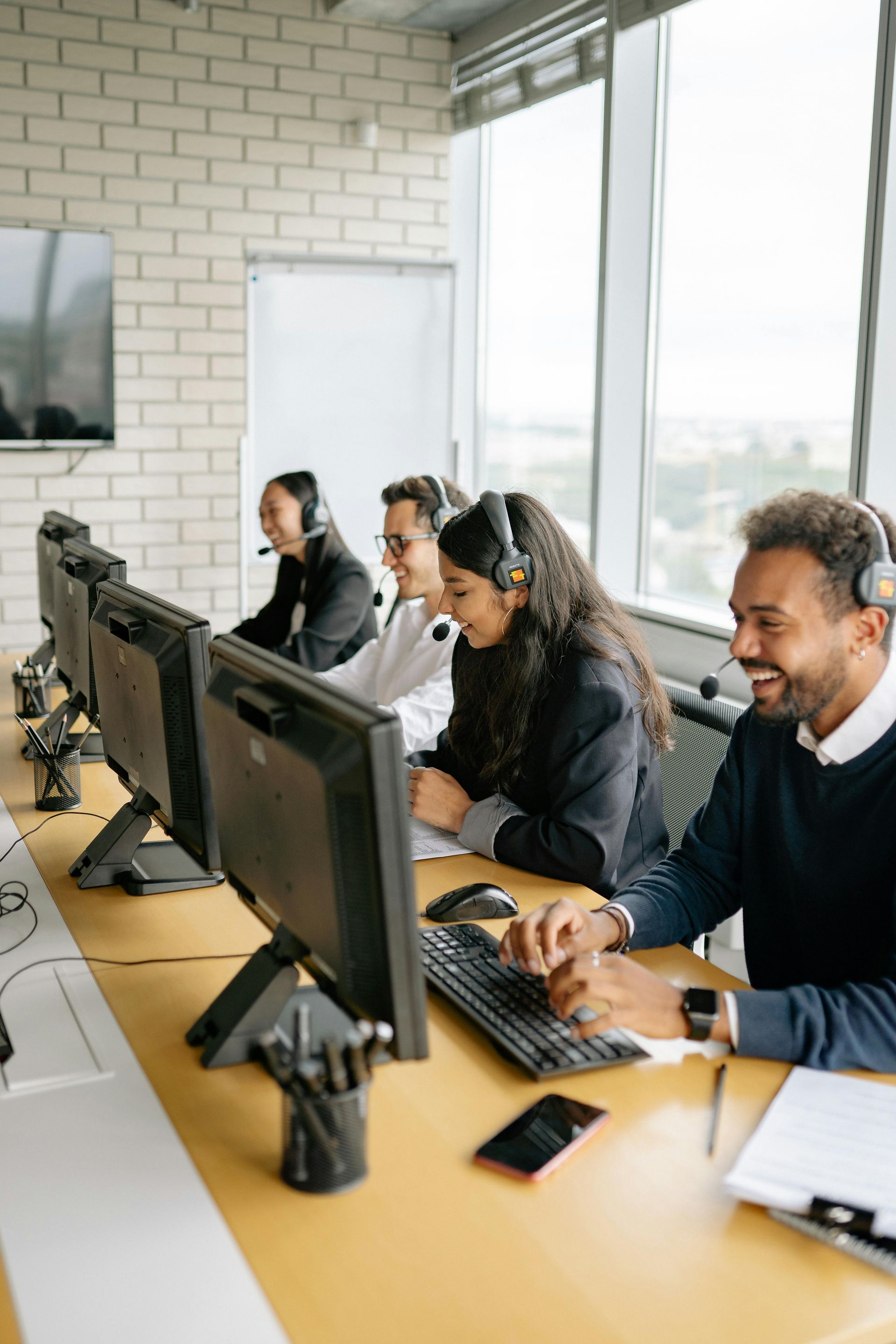 People wearing headsets working at desktop computers in a bright office.