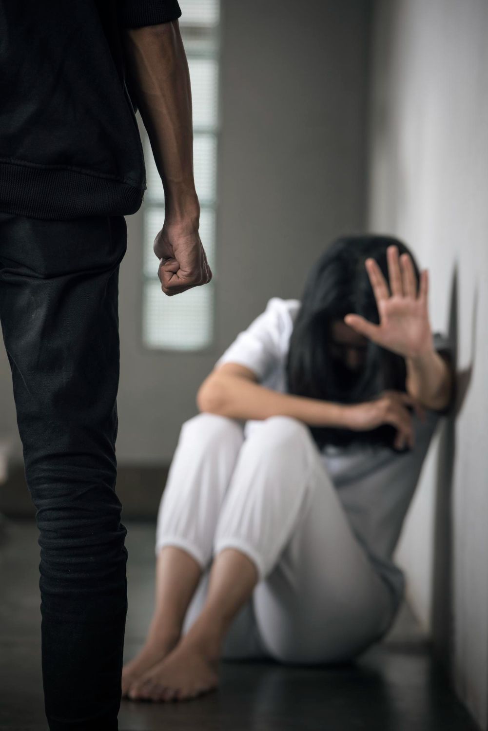 Person raises fist toward person on the floor, hand raised in defense. Scene in a hallway.