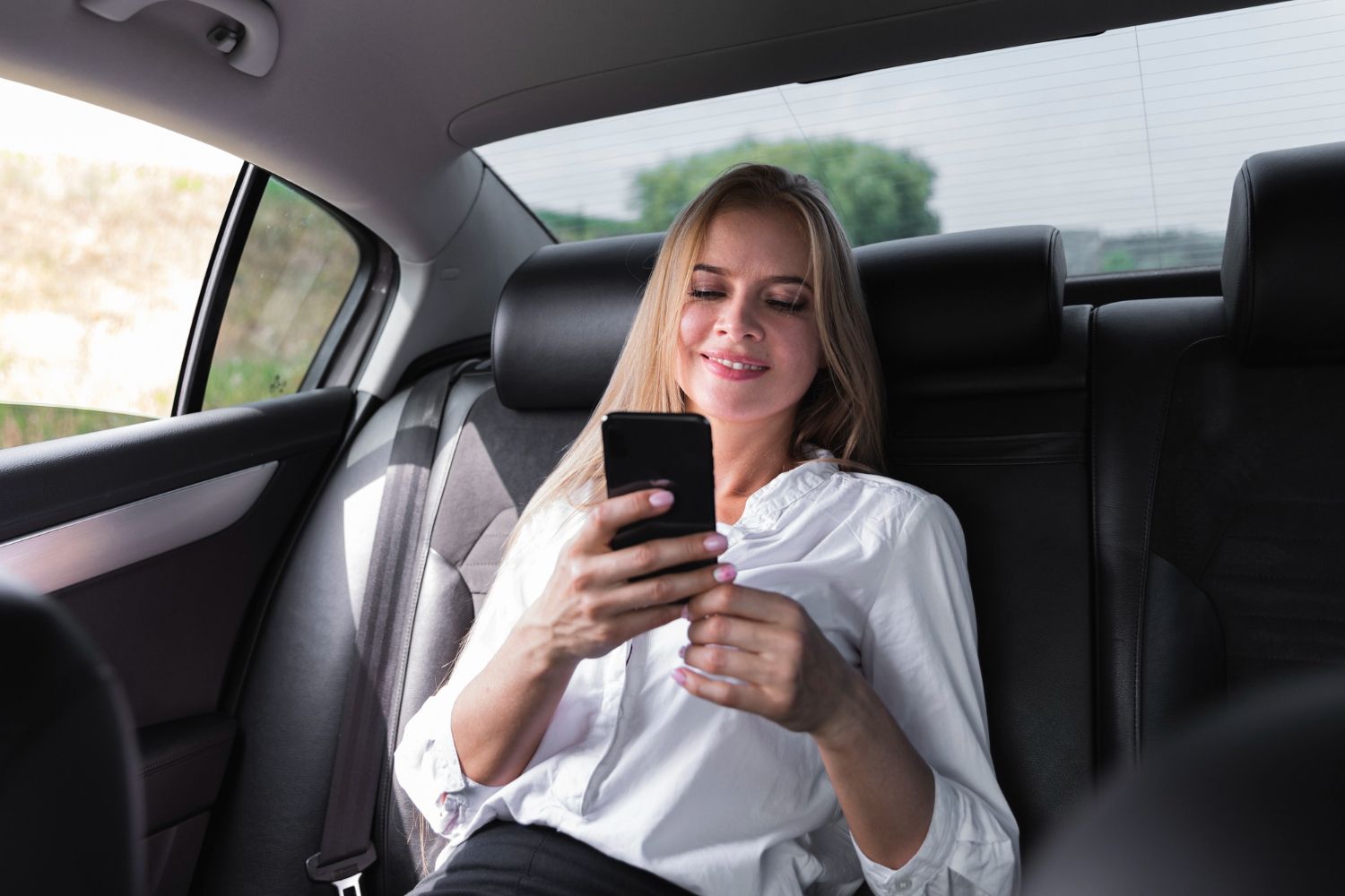 Woman in white shirt using a smartphone in the backseat of a car.