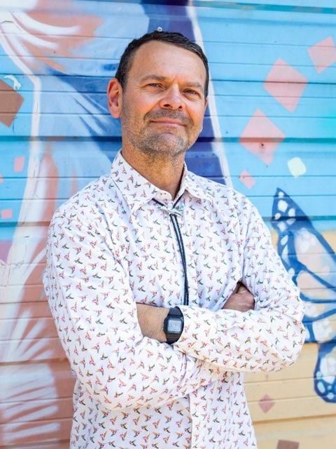 A man is standing in front of a graffiti wall with his arms crossed.