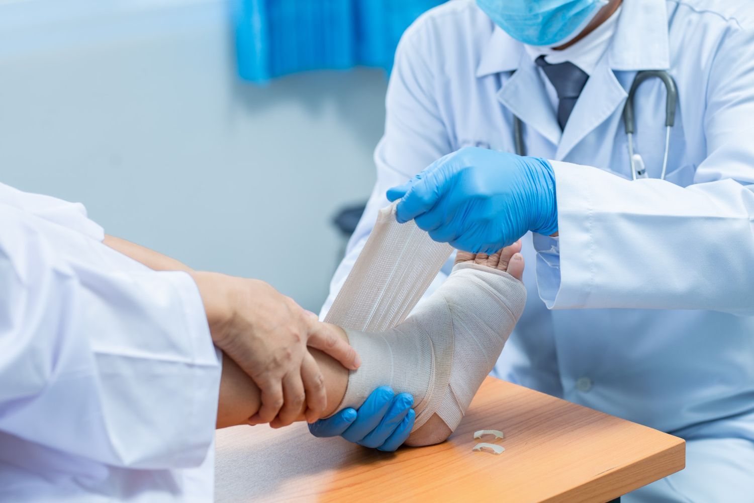 Doctor bandaging patient's foot with a cast in a medical setting. Blue gloves, white coat, light background.