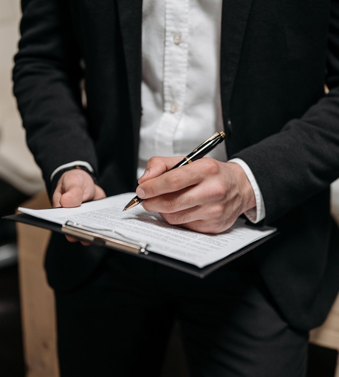 A man in a suit is writing on a clipboard with a pen.