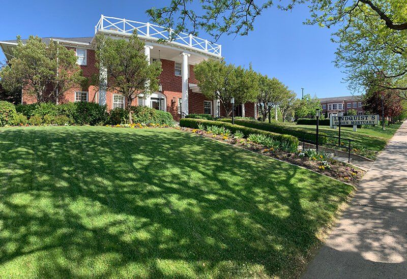 A large brick building with a balcony on top of it is surrounded by trees and grass.