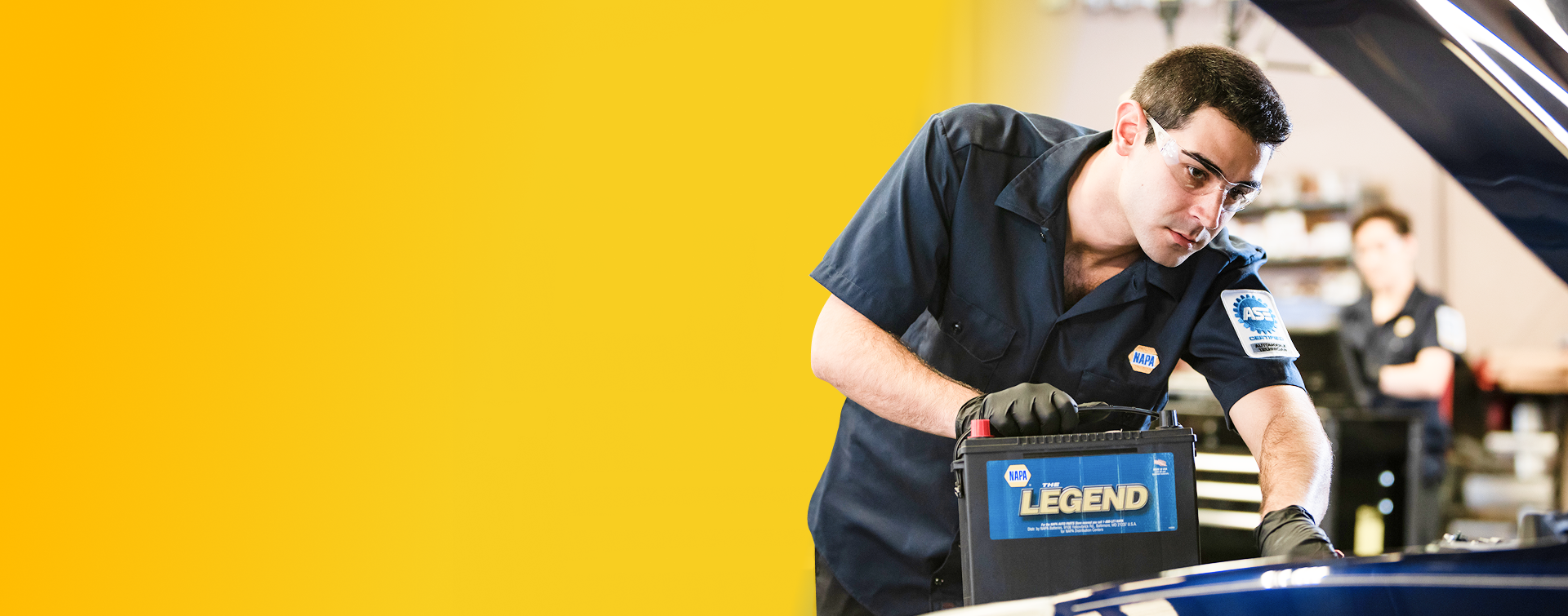 Mechanic replacing a car battery in a garage, holding a NAPA Legend battery. | AAA Full Service Auto Care