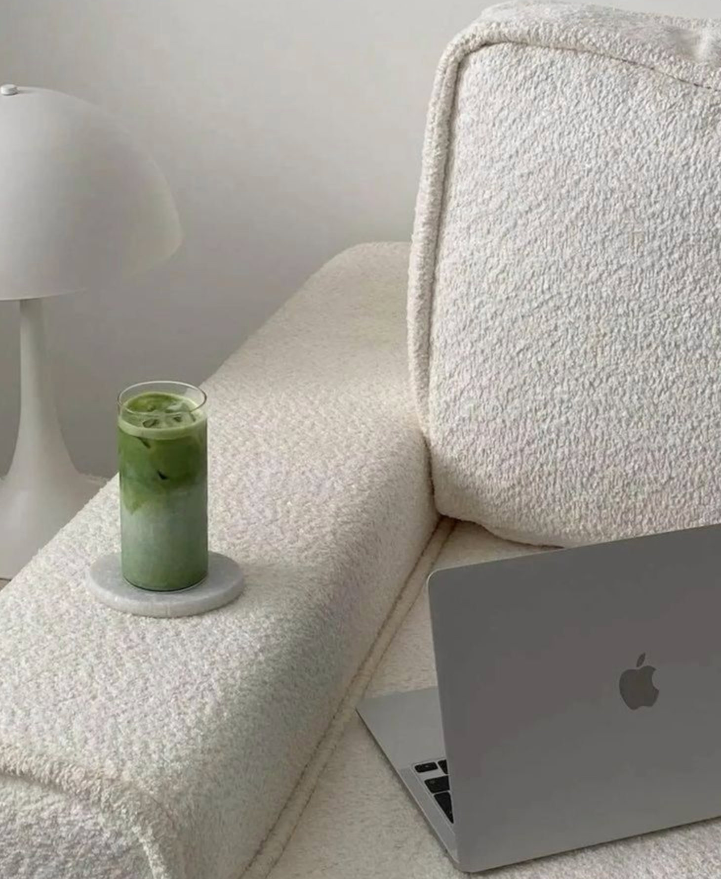 Un ordinateur portable et un verre de matcha posés sur un canapé blanc.