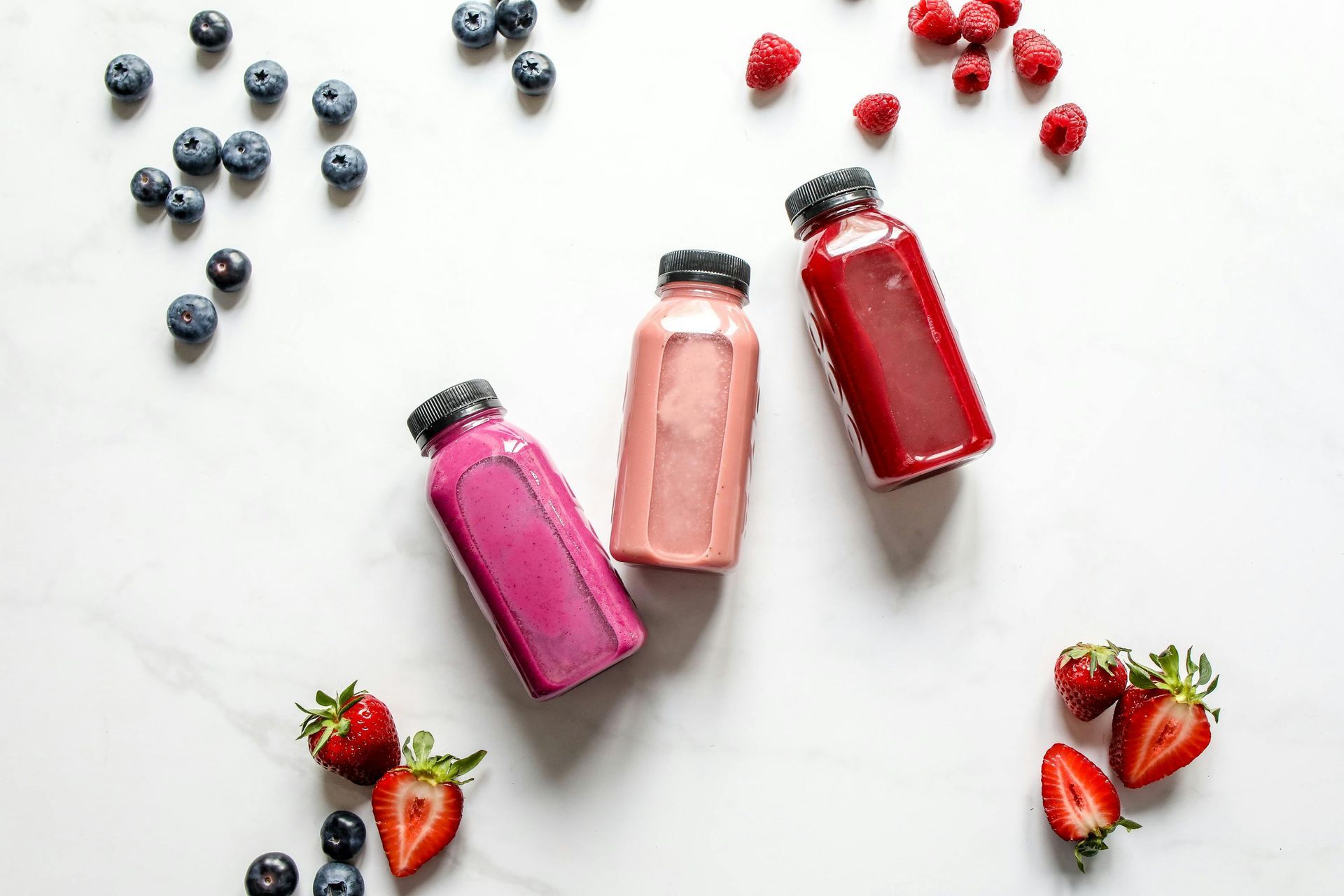Three bottles of smoothies and berries on a table.