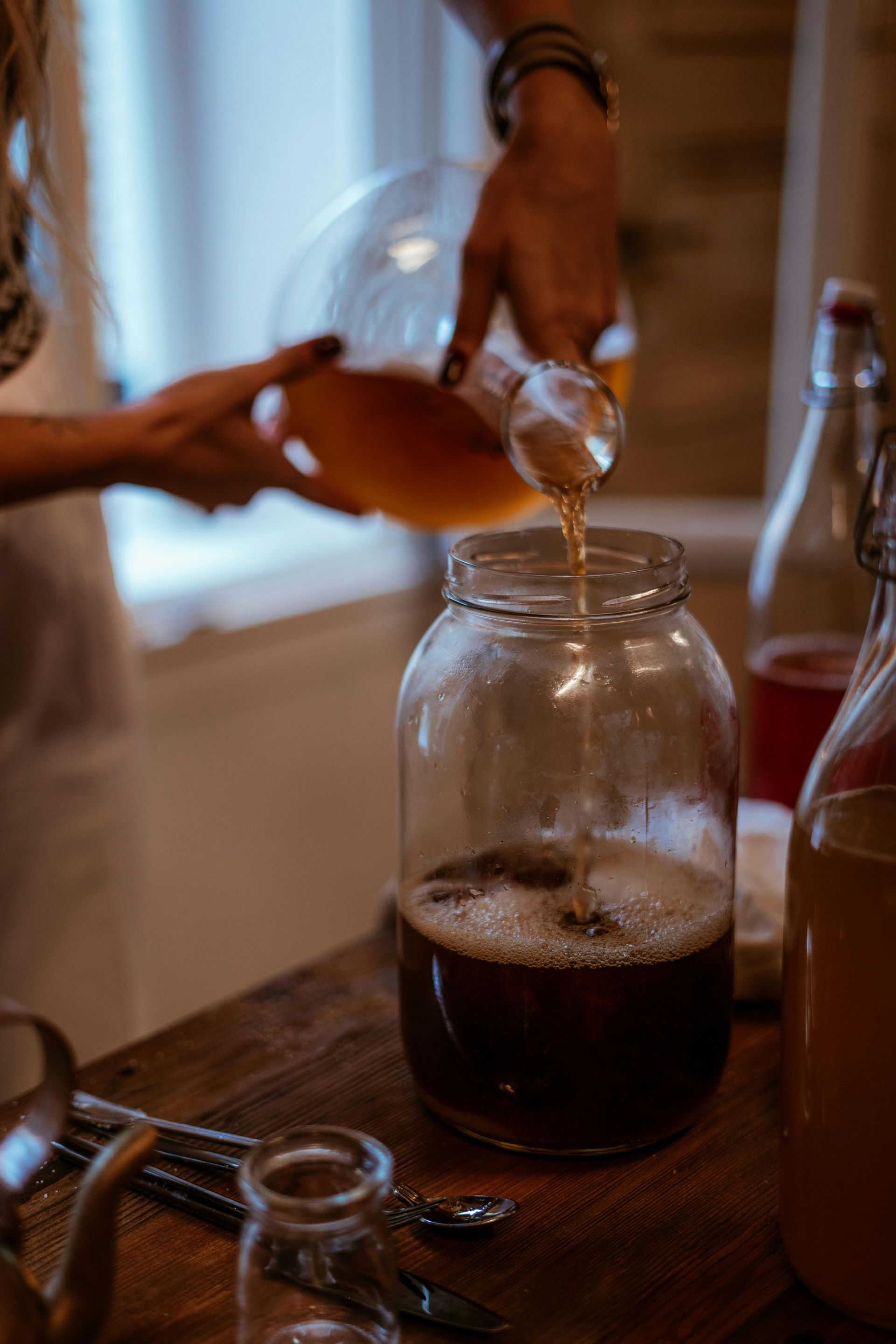 Une personne verse du kombucha dans un bocal sur une table.