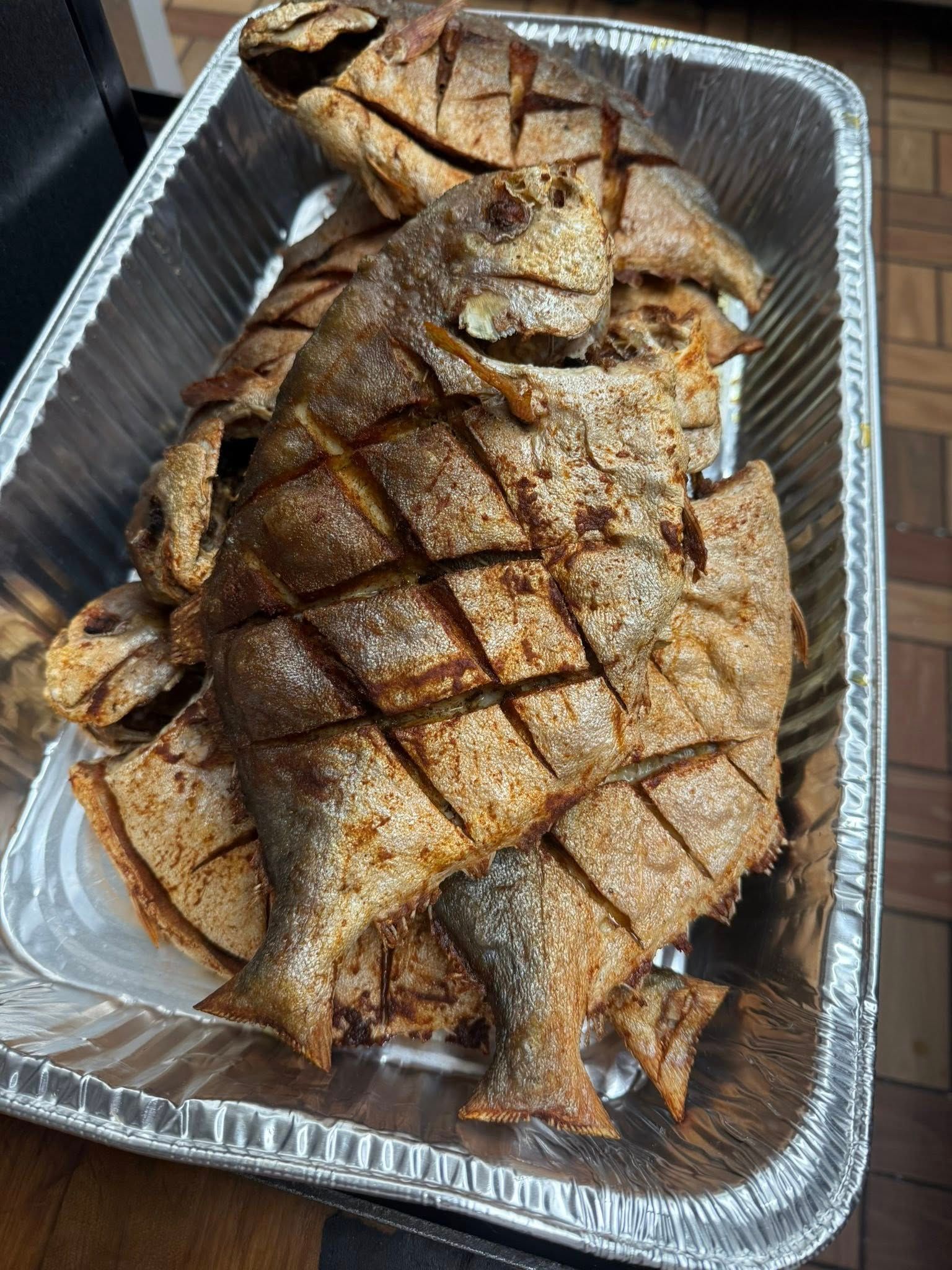 Fried fish in a silver foil container, cut with diamond patterns.