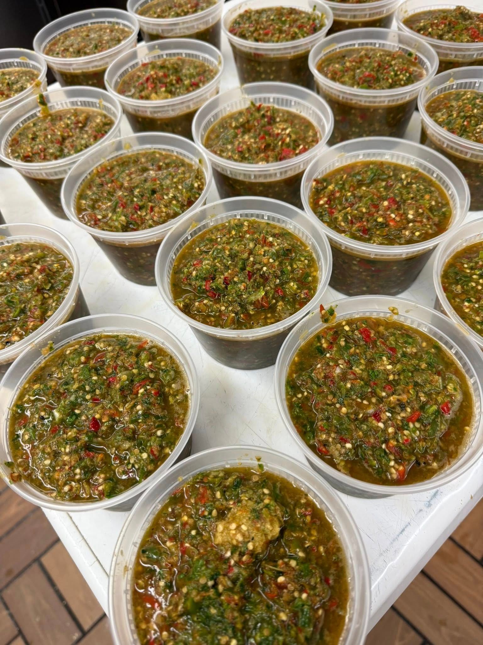 Containers of green and red speckled sauce on a white table.