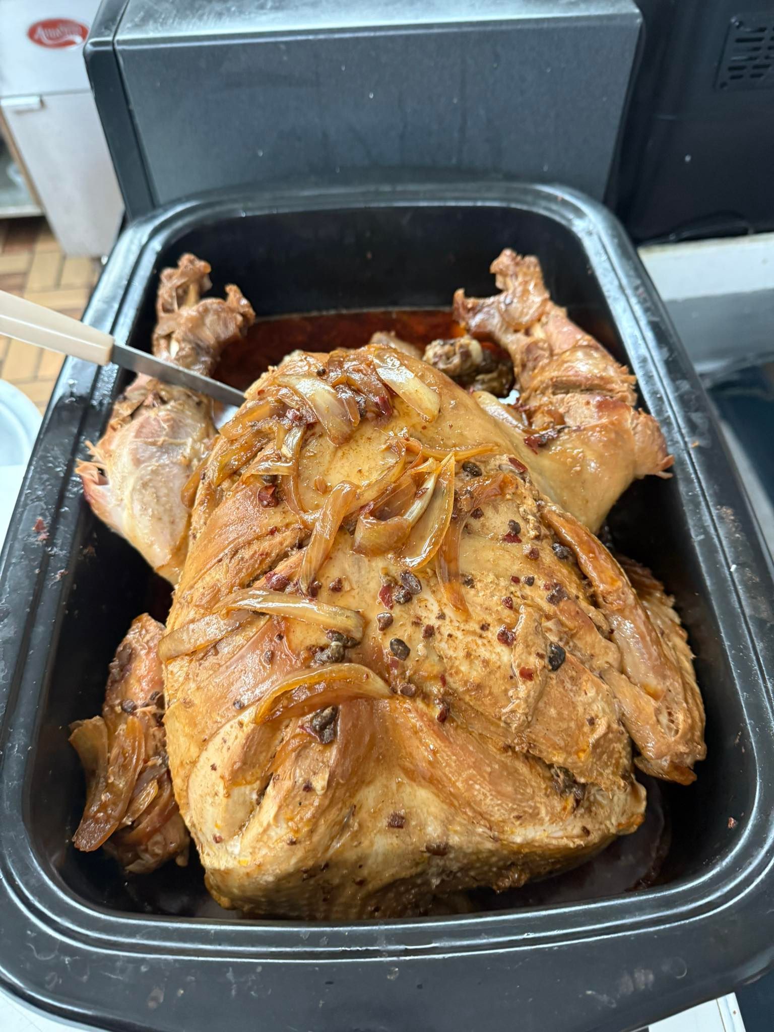 Roasted chicken in a black roasting pan, topped with onions and spices.