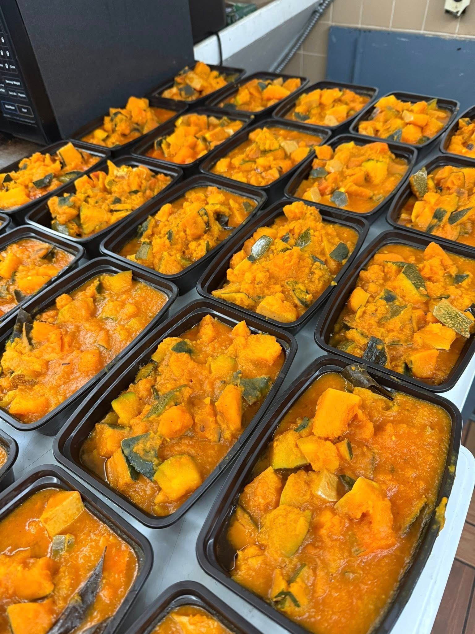 Many individual black containers filled with orange and green food, likely cooked squash or pumpkin.