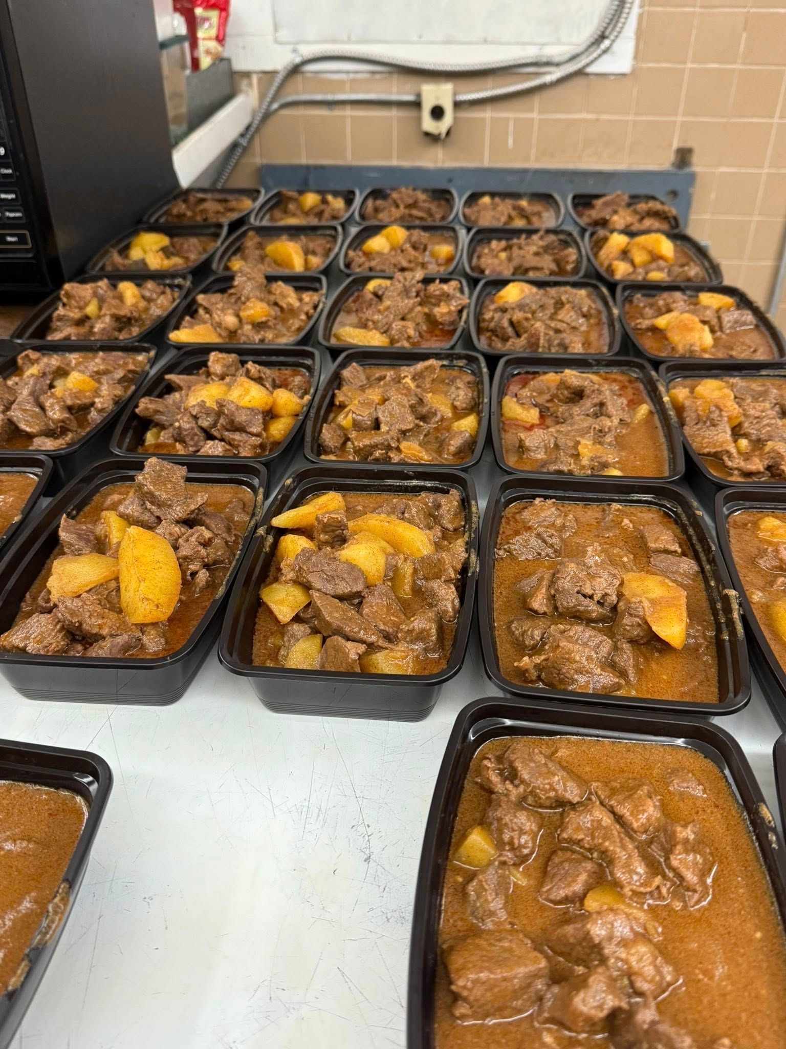 Prepared meals in black containers, stew with meat and potatoes.