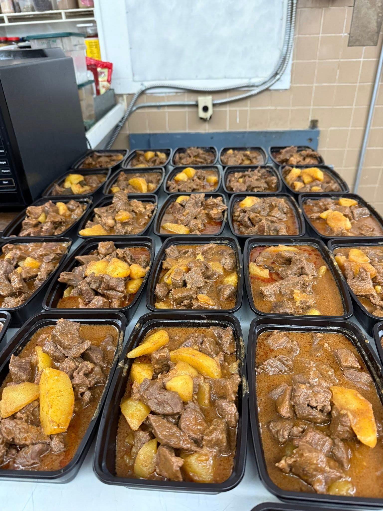 Prepared meals of meat and potatoes in black containers, ready for serving.