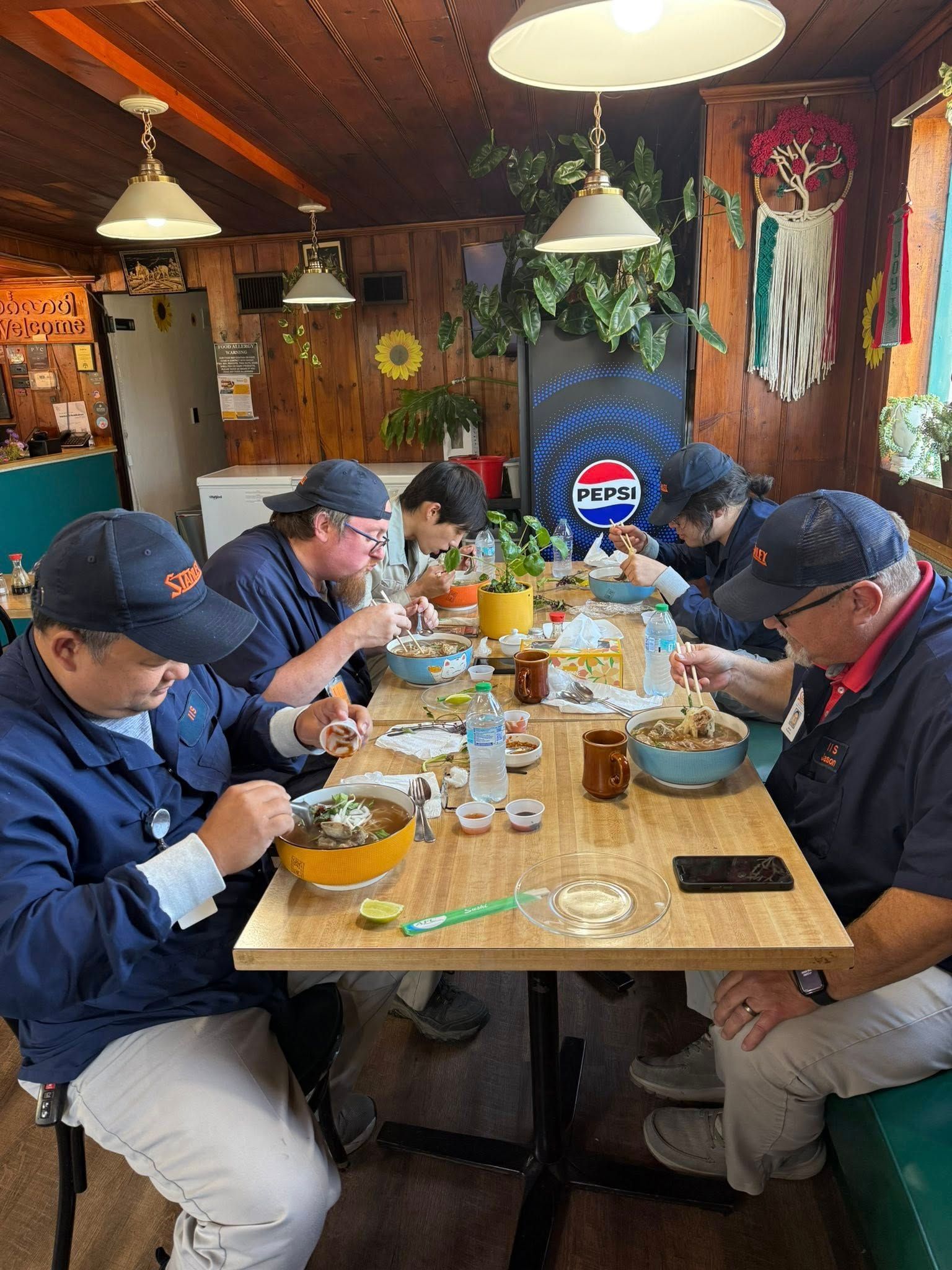 Group of people in blue shirts eating at a wooden table in a diner.
