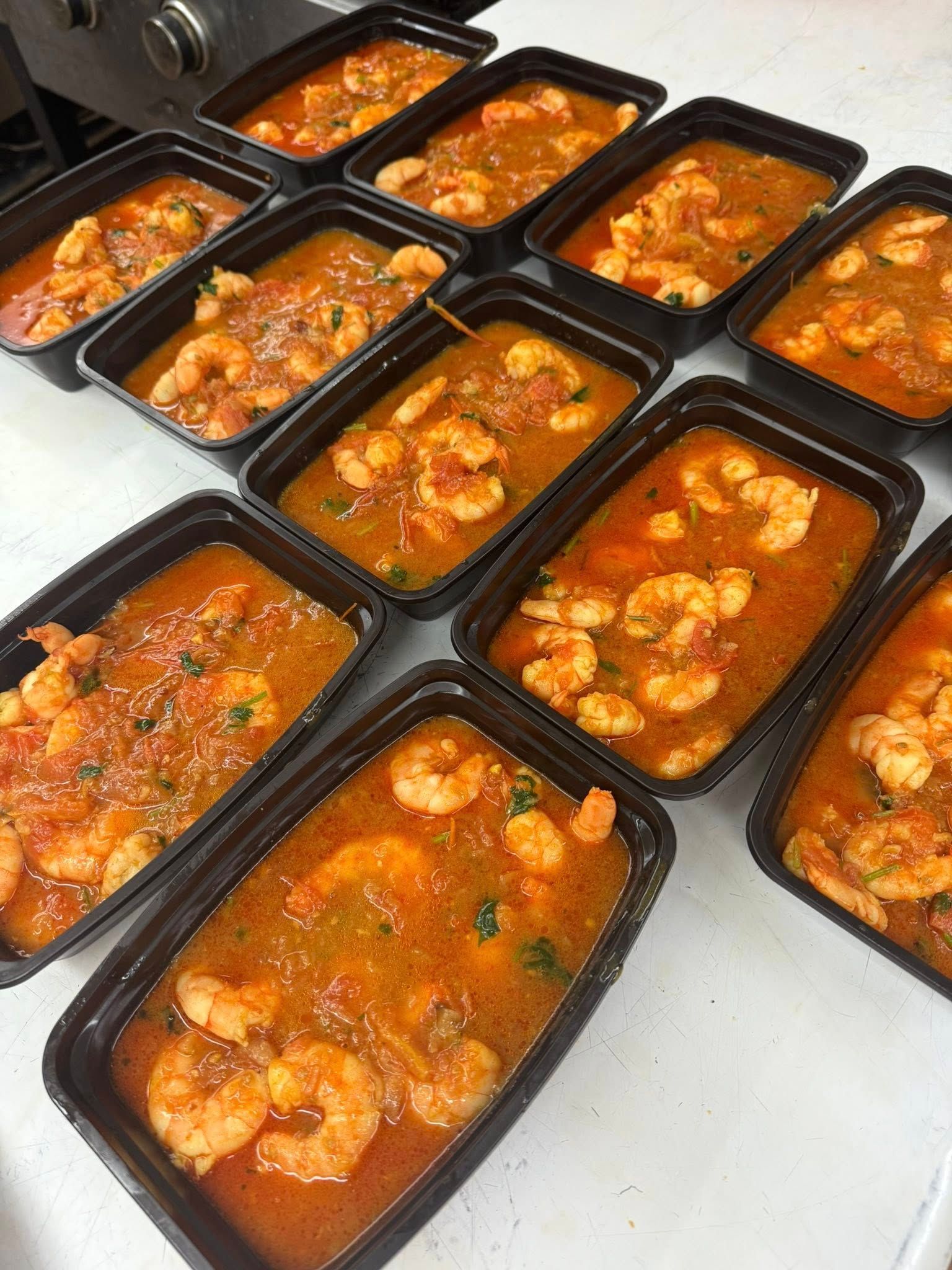 Containers of shrimp in a red sauce, prepared for takeout or meal prep.