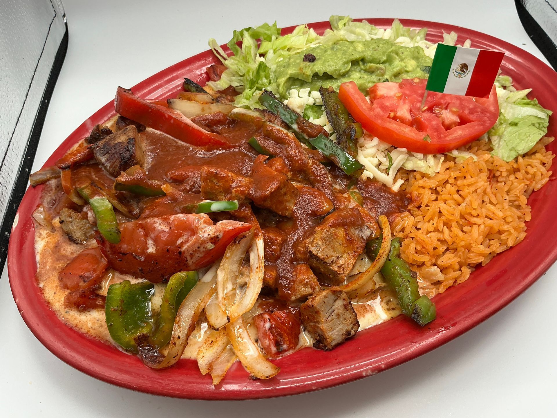 Red plate with Mexican food: enchiladas, rice, lettuce, tomato, and peppers on a table