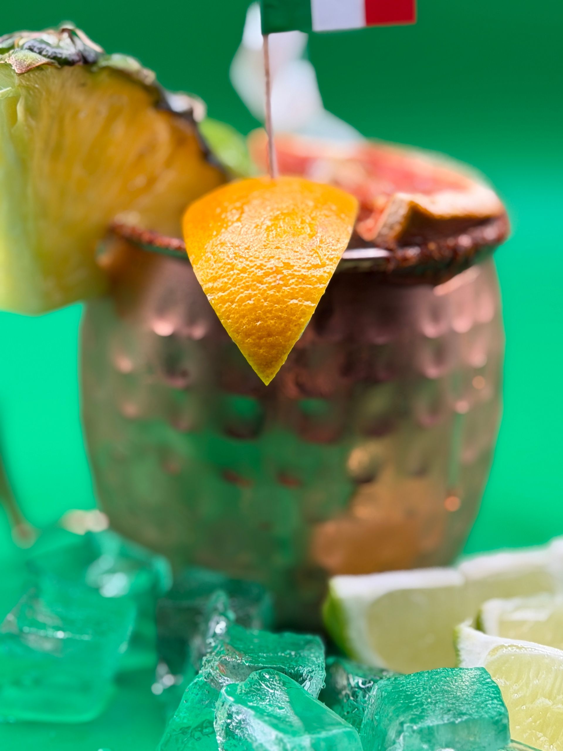 Rustic cup with a lime wedge and mint on a green tabletop, festive drink close-up