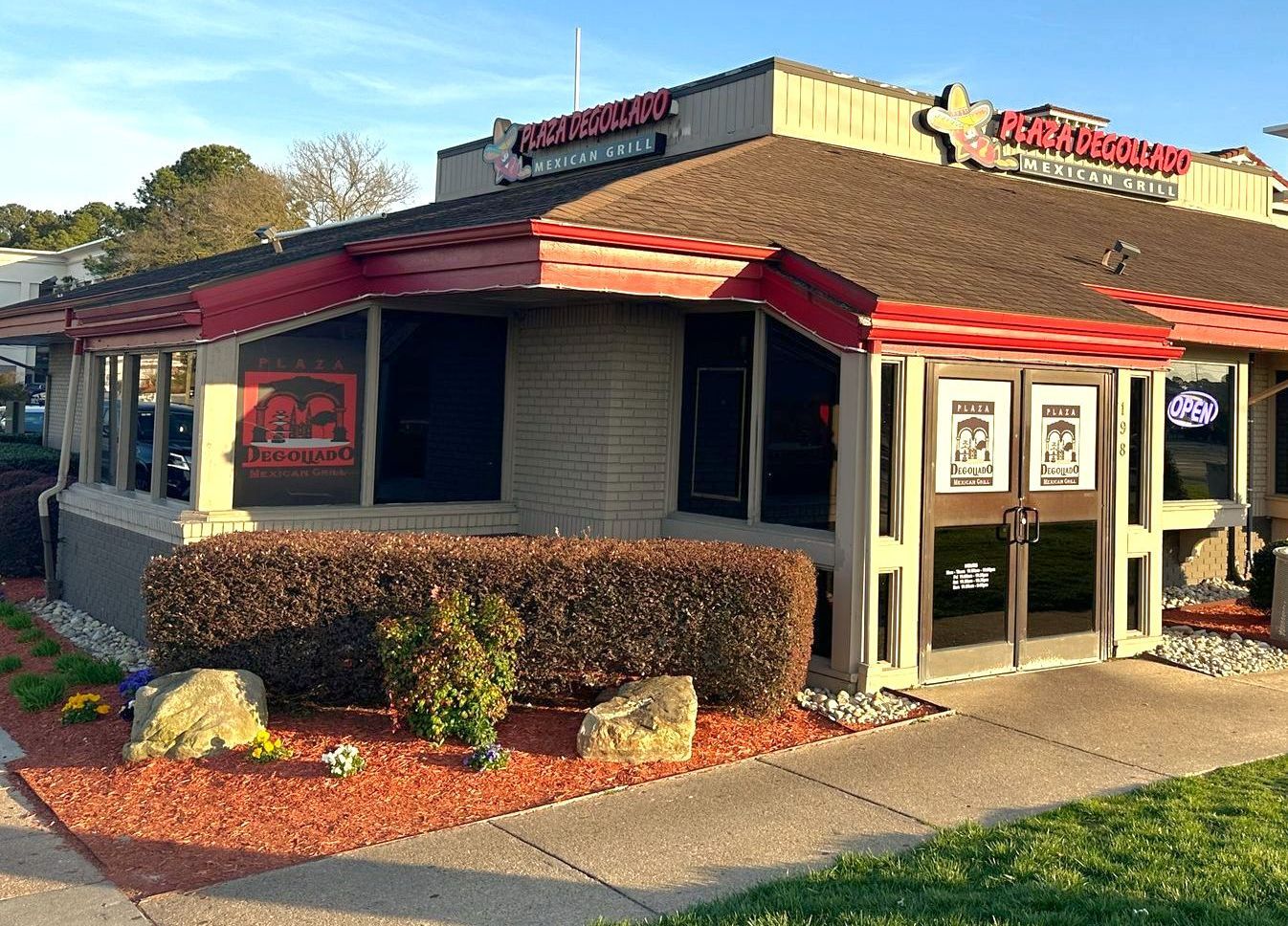 Low, red-roofed fast-food restaurant with outdoor windows and shrubs at sunset