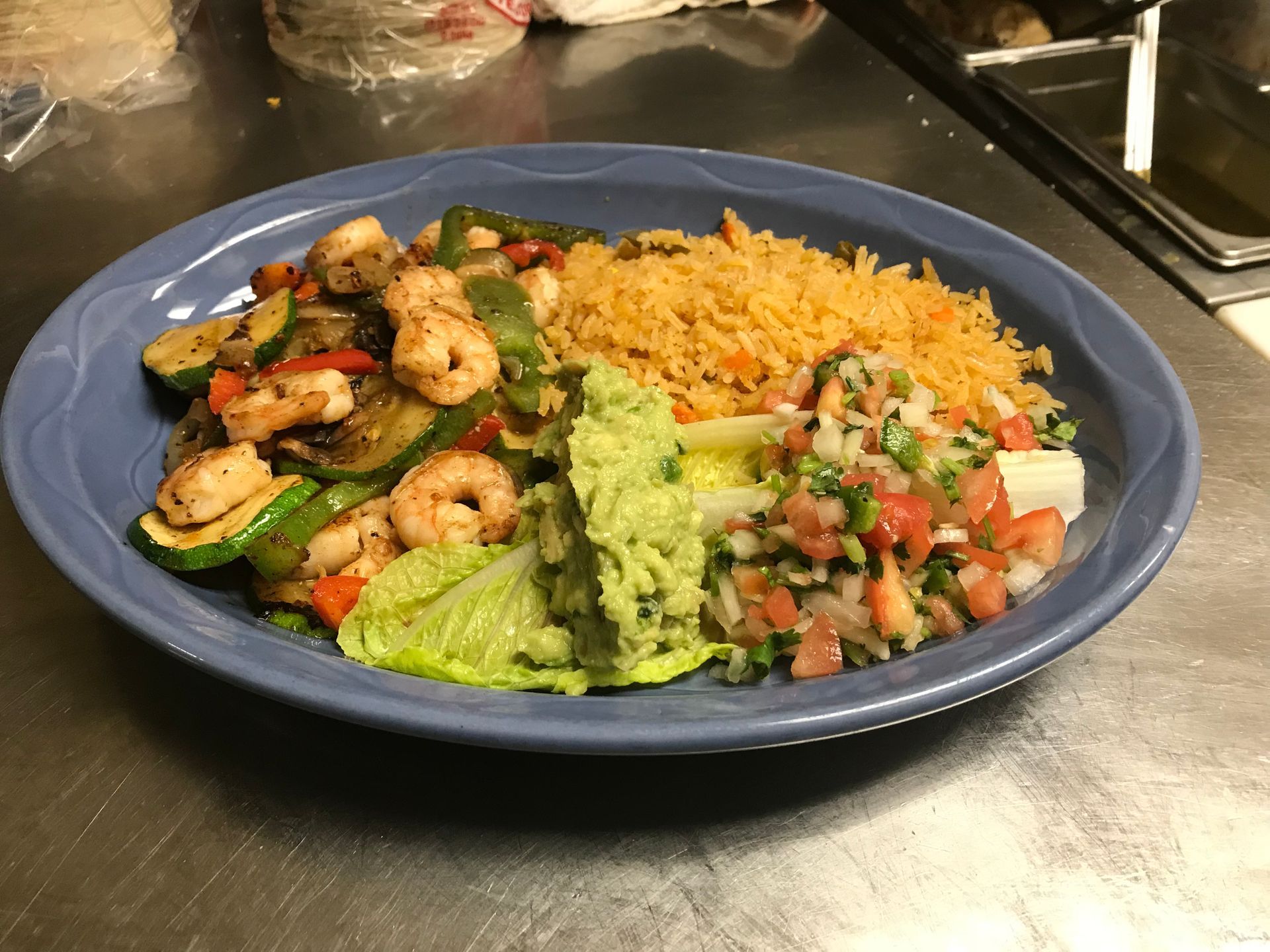 Shrimp fajitas with rice, guacamole, and pico de gallo on a blue plate.