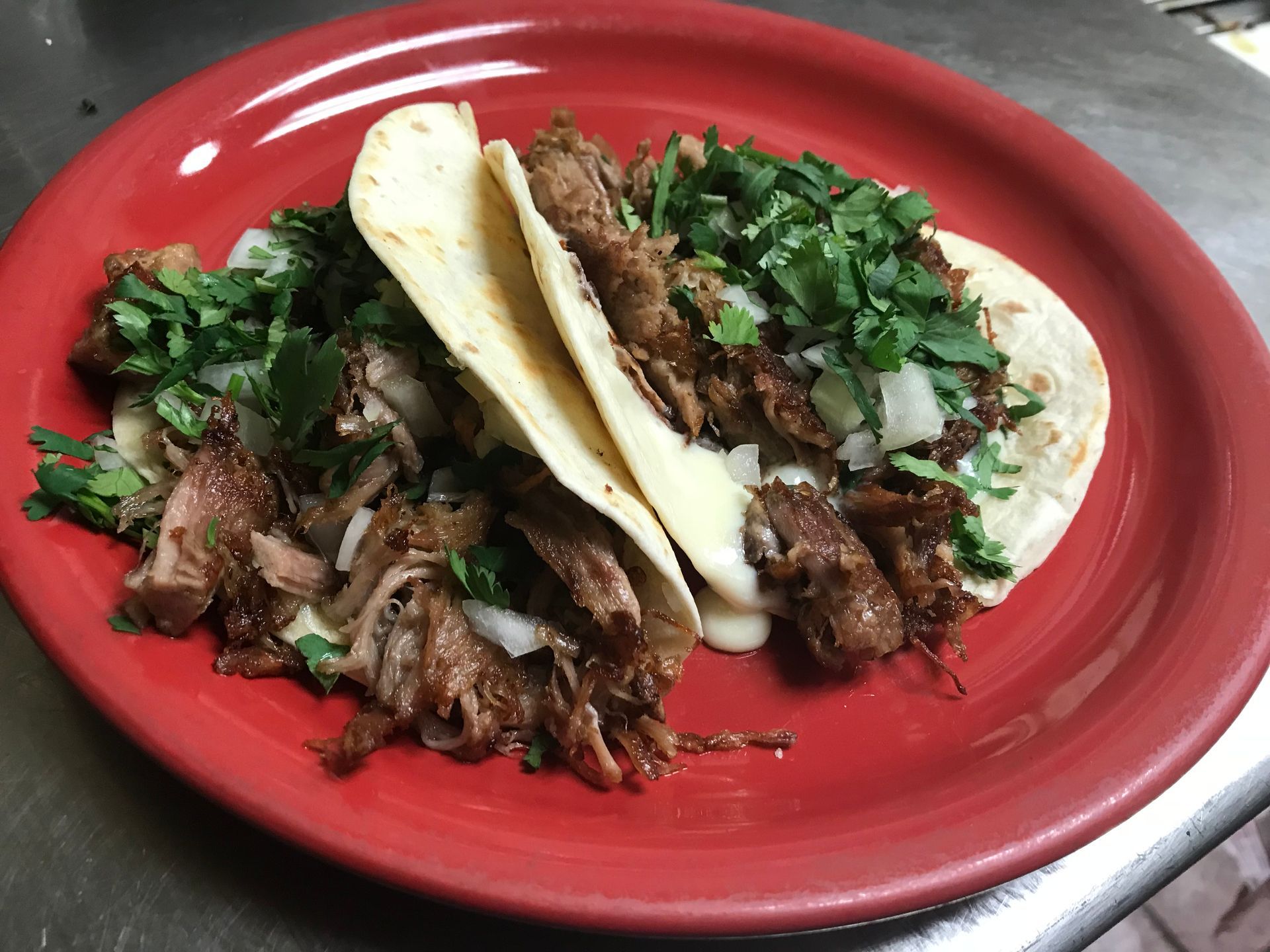 Two tacos on a red plate with meat, onions, and cilantro.