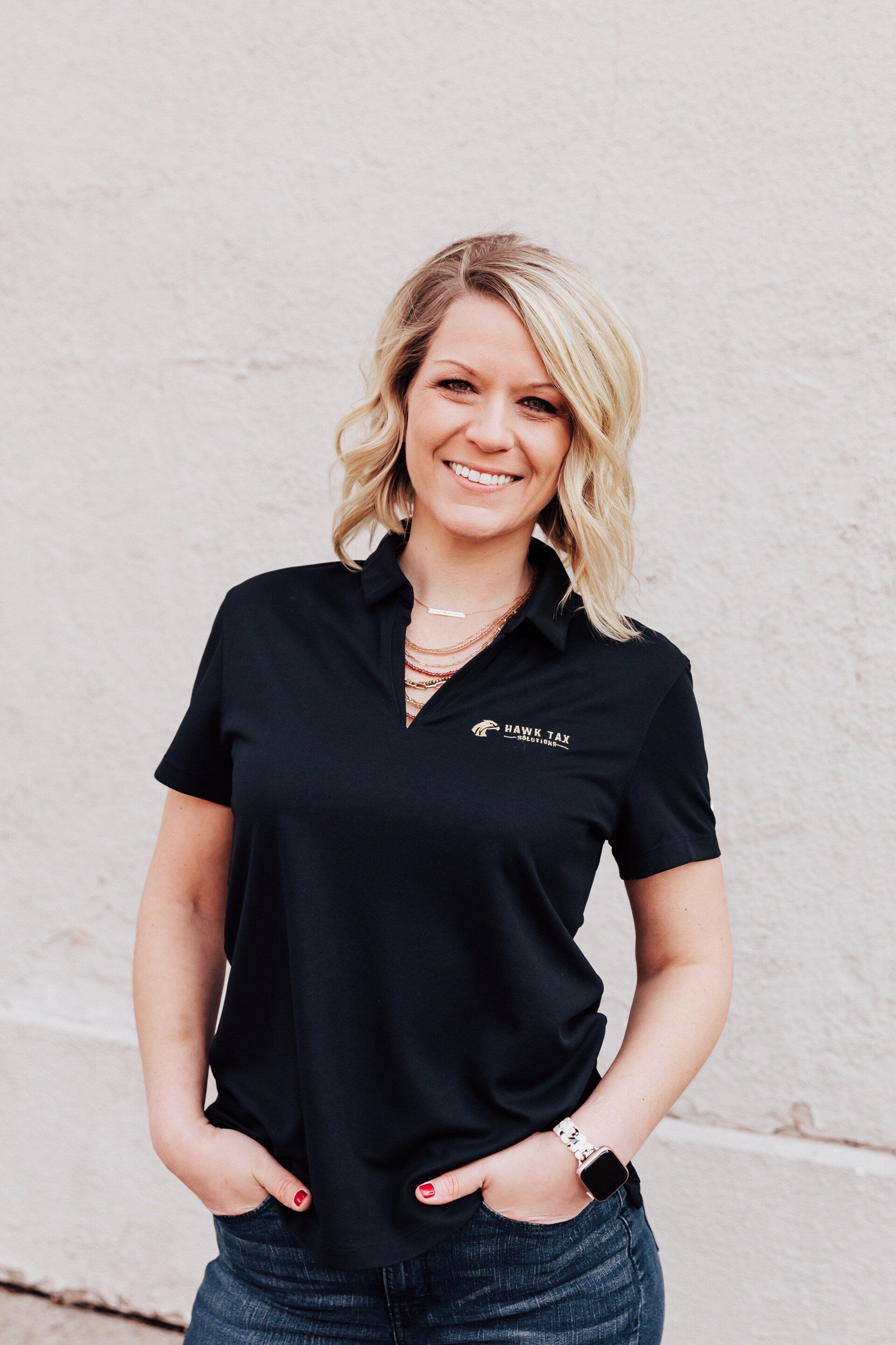 a woman wearing a black polo shirt and jeans is standing in front of a white wall .