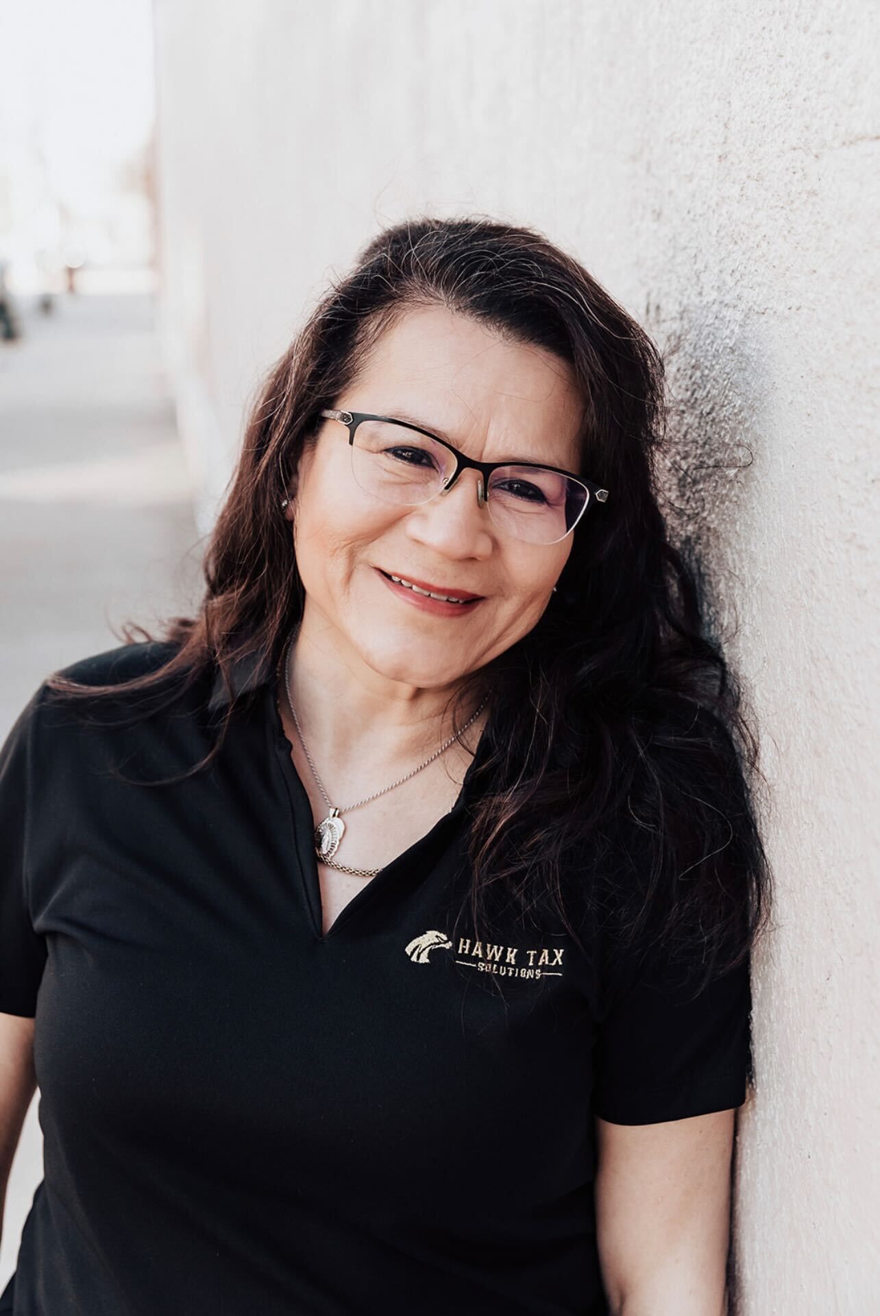 a woman wearing glasses and a black shirt is leaning against a wall .