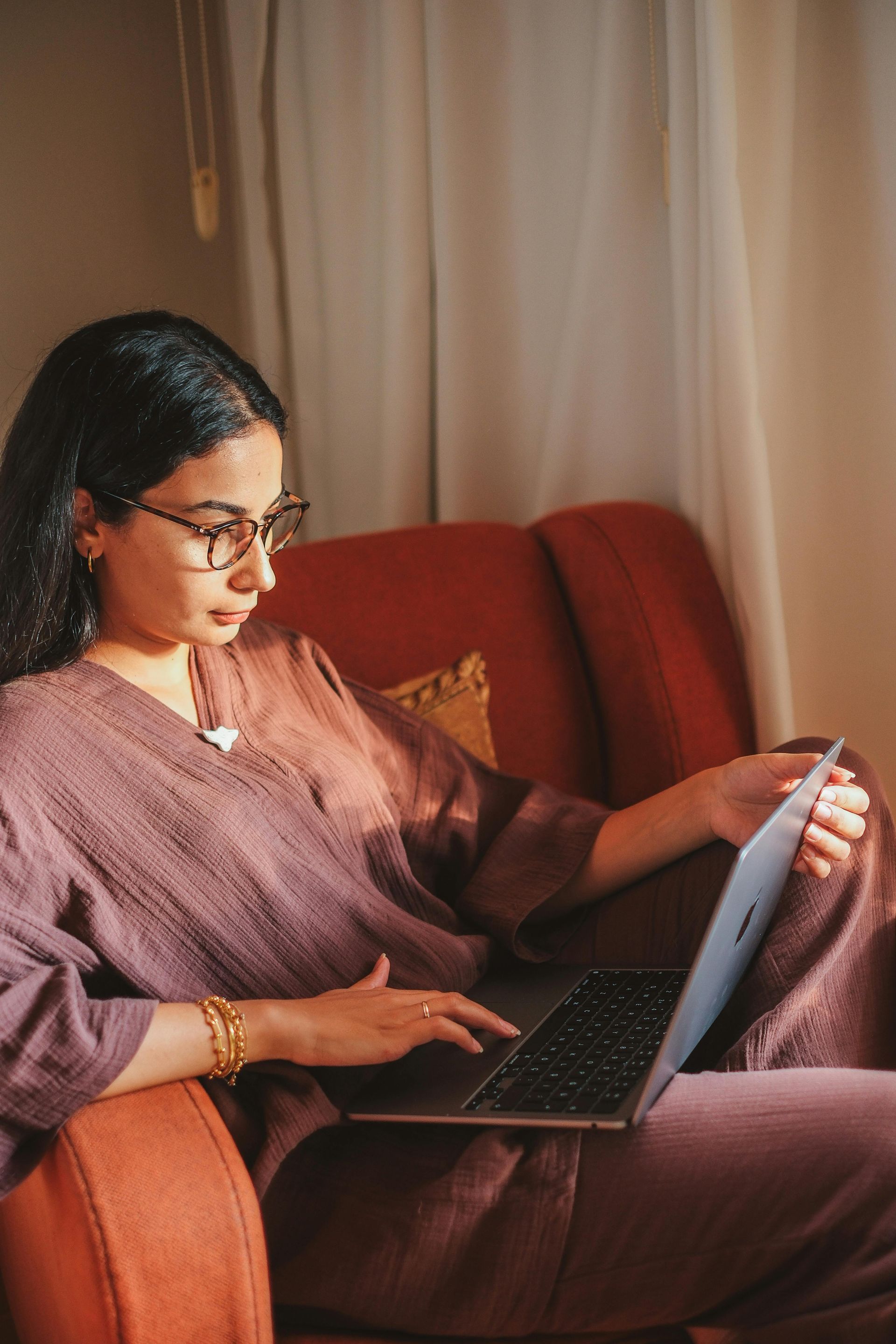 A woman is sitting on a couch using a laptop computer to file taxes.