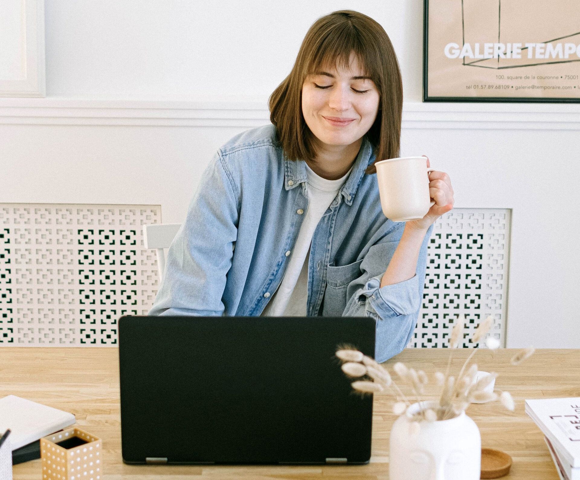 Smiling woman on laptop drinking coffee out of a white mug
