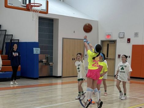 Basketball players in white and neon jerseys jump for a shot in a gymnasium.