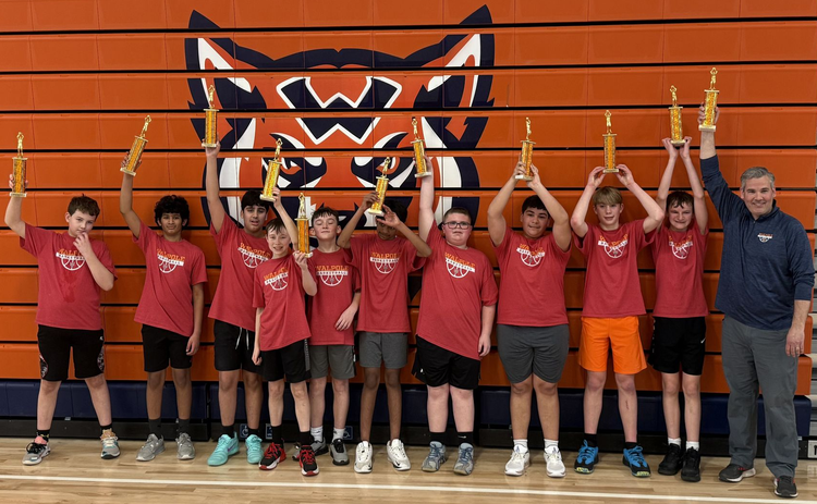 Youth volleyball team in red jerseys holding trophies in a gym with an orange wall logo