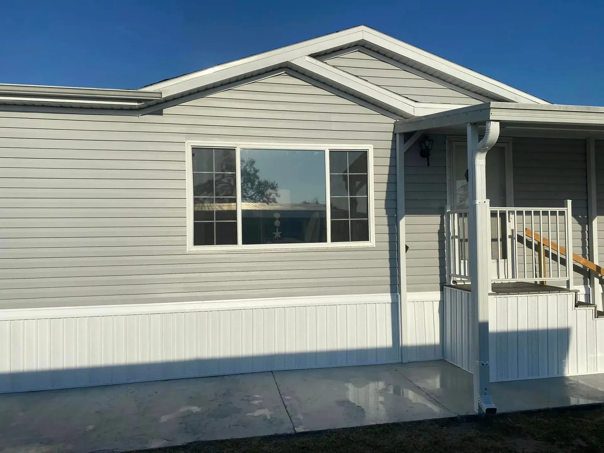 Light gray mobile home with white trim and a concrete patio.