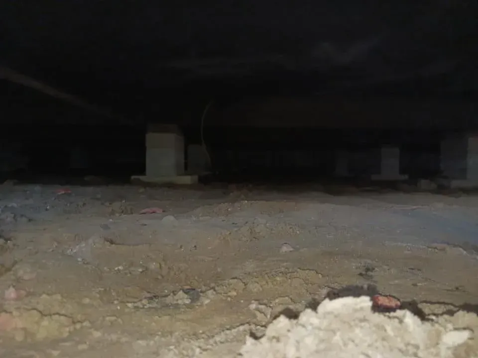 Dark crawlspace with concrete piers supporting a wooden floor.