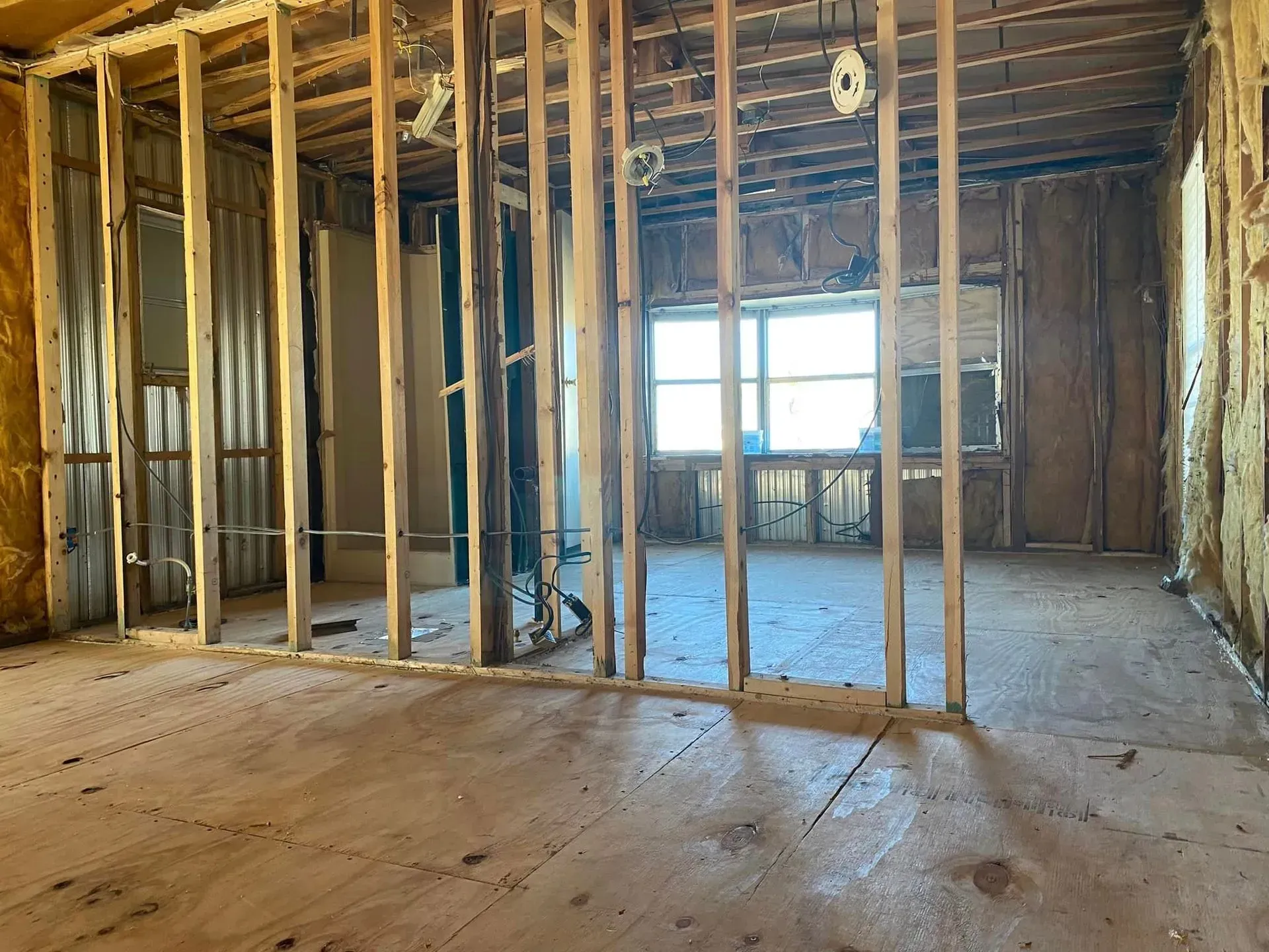 Interior view of a room under construction, with exposed wooden studs, window, and flooring visible. Interior view of a room under construction, with exposed wooden studs, window, and flooring visible.