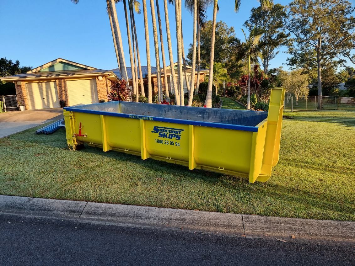 Yellow skip bin on the grass next to a house — Suncoast Skips in Coolum Beach, QLD