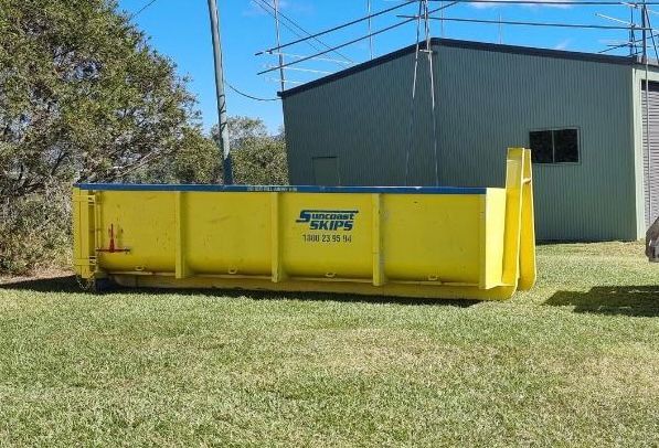 Large yellow hook bin on the grass next to a shed — Suncoast Skips in Coolum Beach, QLD