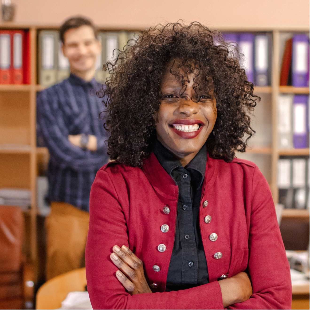A woman in a red jacket is smiling in front of a man in a plaid shirt.