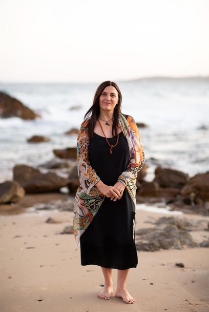 Turquoise ocean meets sandy beach under a bright blue sky with clouds, buildings on the horizon.