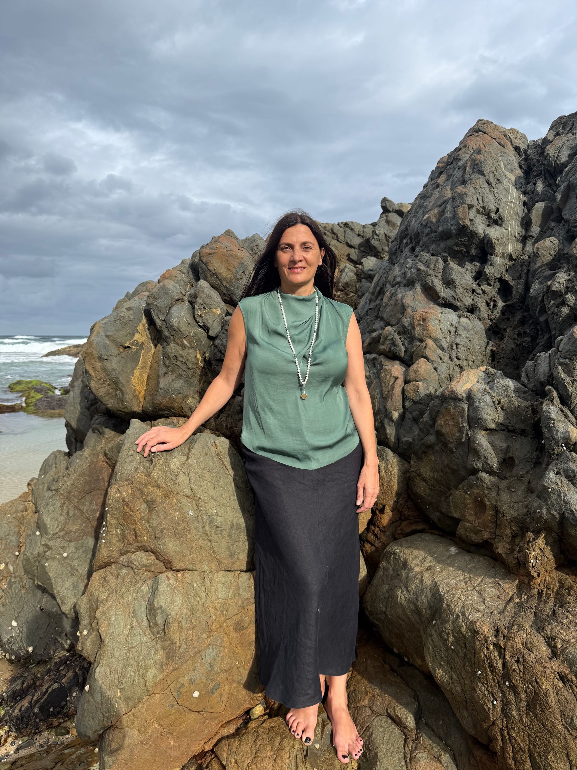 A person sits calmly with eyes closed on a rocky beach by the ocean — Vedic Meditation & Coherence Personal Counselling in Coffs Harbour, NSW