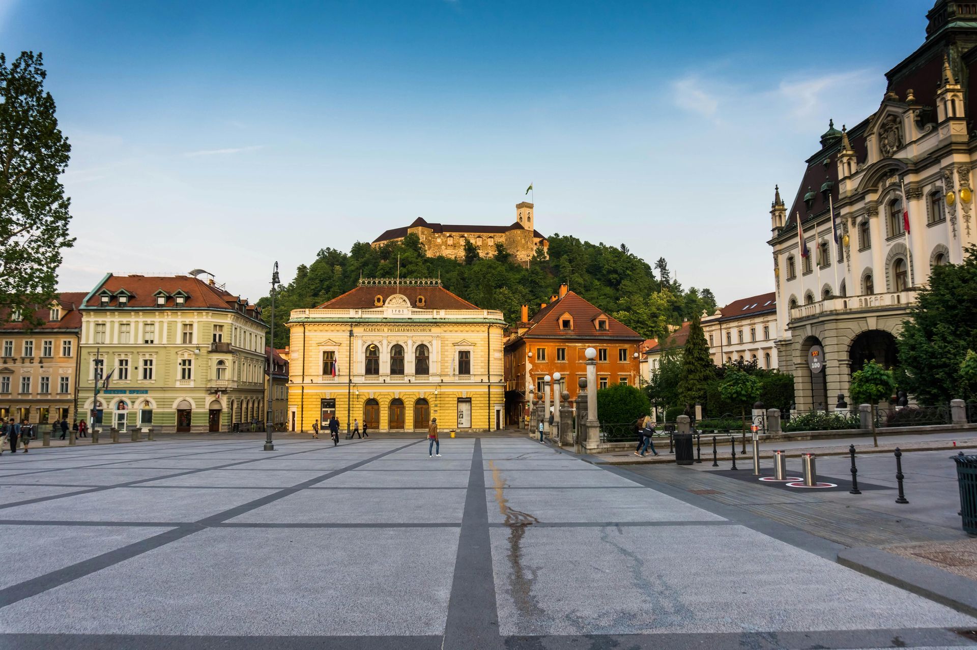 Large empty square with buildings, a hilltop castle, and a clear blue sky in Ljubljana, Slovenia.