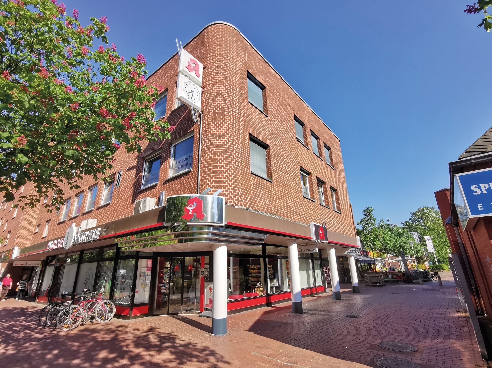 Auf einem gemauerten Gehweg steht ein großes Backsteingebäude mit vielen Fenstern.